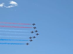 Záběr na devítičlennou formaci Red Arrows zanechávající za sebou typickou červeno-bílo-modrou kouřovou stopu.